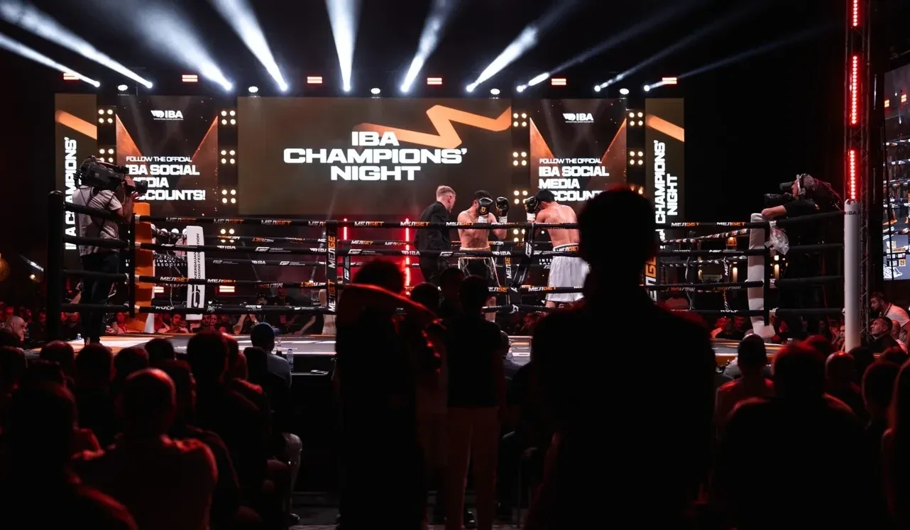Ринг IBA Champions’ Night вечером: экраны с названием турнира, лучи прожекторов и зрители у канатов